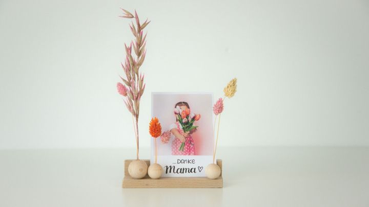 Ein Holz-Kartenhalter pr&auml;sentiert ein Foto eines M&auml;dchens mit Blumen und der Aufschrift &bdquo;Danke Mama &hearts;&ldquo; in einem hellen Raum.