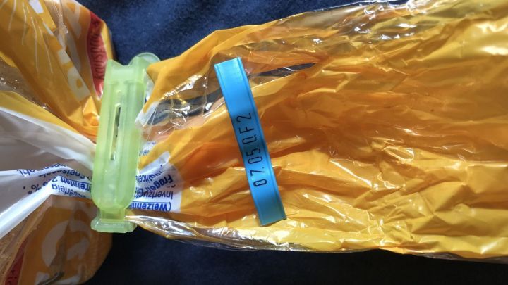 Ein gelber Toastbrotsack mit einem Clipband, das das Mindesthaltbarkeitsdatum "07.05.0F2" anzeigt, liegt auf einem dunklen Untergrund.