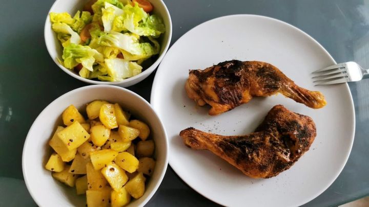 Gegrillte H&auml;hnchenschenkel auf einem Teller, umgeben von Salat und gew&uuml;rzten Kartoffeln, appetitlich angerichtet.