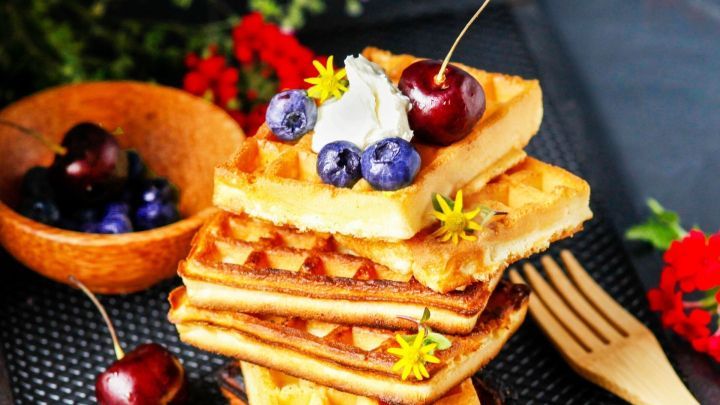 Waffeln stapeln sich mit frischen Beeren und einer Kirsche, auf einem rustikalen Hintergrund mit Naturdetails.