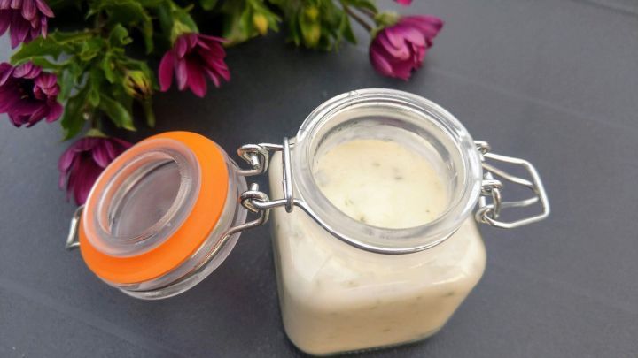 Ein Glas mit Spargelbutter steht offen auf einem Tisch, umgeben von lila Blumen, die Frische ausstrahlen.