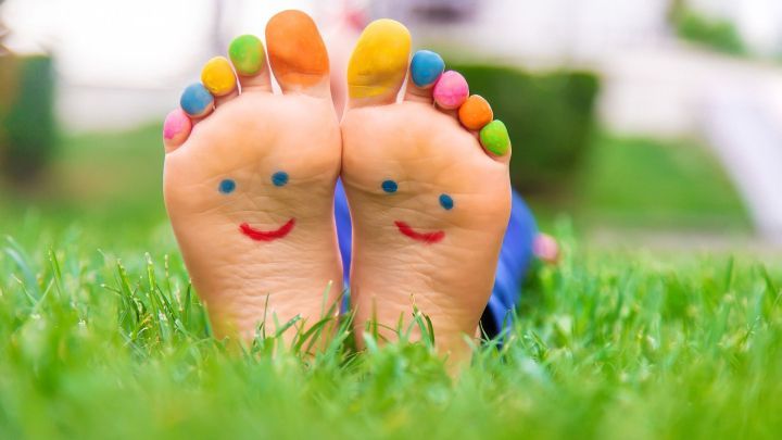 Barfu&szlig;f&uuml;&szlig;e mit bunten Zehen sind auf gr&uuml;nem Gras sichtbar und l&auml;cheln freundlich in die Kamera.