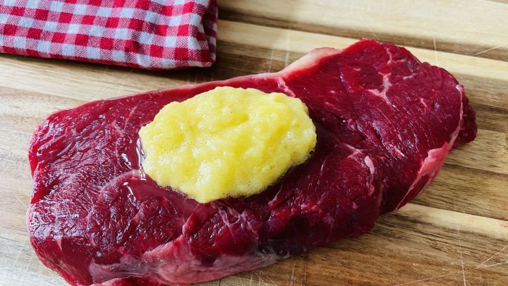 Saftiges Steak liegt auf einem Holzbrett, bedeckt mit einer Ananas-Marinade und einem karierten Tuch im Hintergrund.
