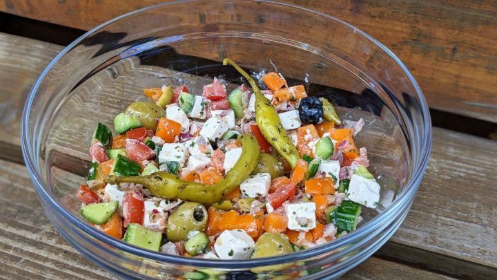 Ein bunter gemischter Salat aus Gem&uuml;se, Feta und Oliven in einer Sch&uuml;ssel, platziert auf einem Holztisch.
