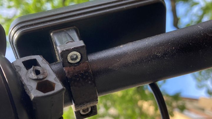 Eine Befestigungsschelle h&auml;lt eine Vorrichtung an einem schwarzen Rohr, umgeben von B&auml;umen und einem blauen Himmel.