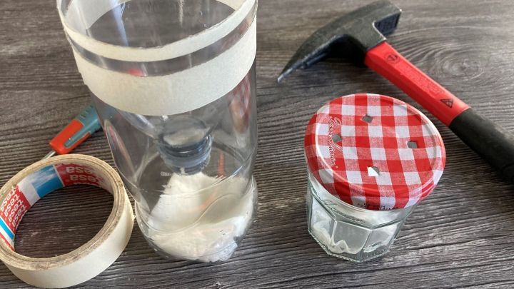 Eine Fliegenfalle wird aus einer plastikflasche, einem Glas und Werkzeugen auf einem Holztisch zusammengestellt.