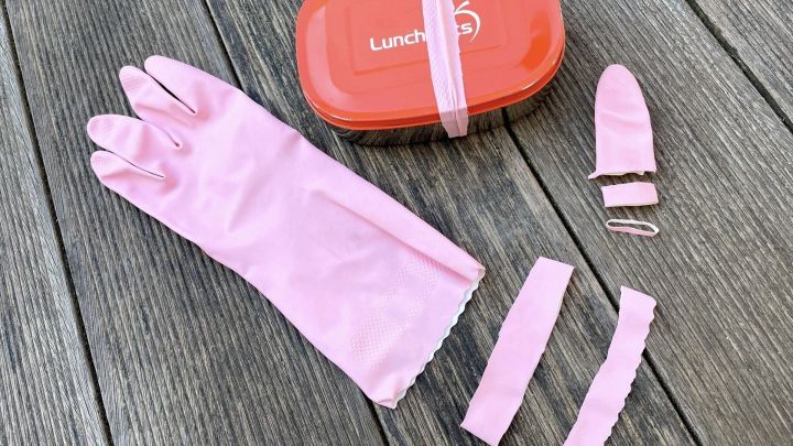 Ein pinker Haushaltshandschuh liegt auf Holzuntergrund, daneben befinden sich Gummiringe und eine Lunchbox.