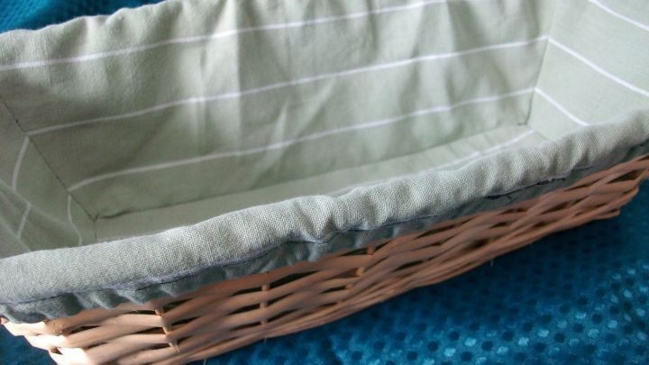 Ein geflochtener Brotkorb mit einer hellgr&uuml;nen, gestreiften Einlage liegt auf einem blauen Tischtuch.