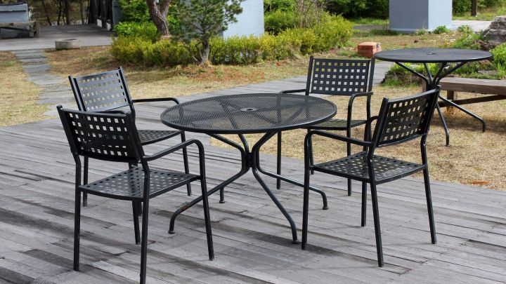 Schwarze Metallgartenm&ouml;bel stehen auf einem Holzdeck, umgeben von Gr&uuml;n, bereit f&uuml;r eine Nutzung im Freien.