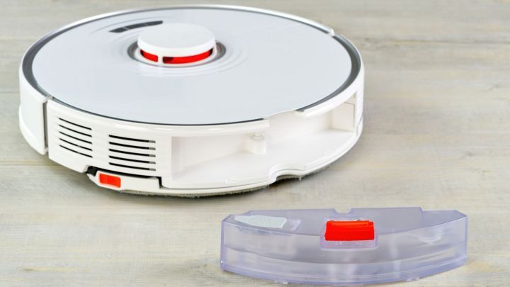 Ein Saugroboter liegt auf einem Holzuntergrund, w&auml;hrend sein abnehmbarer Wassertank daneben platziert ist, bereit zur Reinigung.