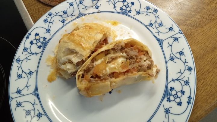 Bl&auml;tterteigrollen sind goldbraun gebacken und gef&uuml;llt mit Fleisch und Gem&uuml;se auf einem Teller neben einer Auflaufform.