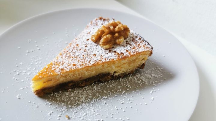 Ein St&uuml;ck Zitronen-Walnuss-Kuchen liegt auf einem wei&szlig;en Teller, mit Puderzucker bestreut und einer Walnuss obendrauf.