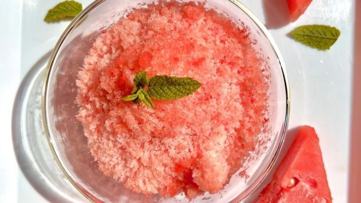 Eine Sch&uuml;ssel mit frischem, rosa Shaved Ice aus Wassermelone ist von Wassertropfen und Melonenst&uuml;cken umgeben.