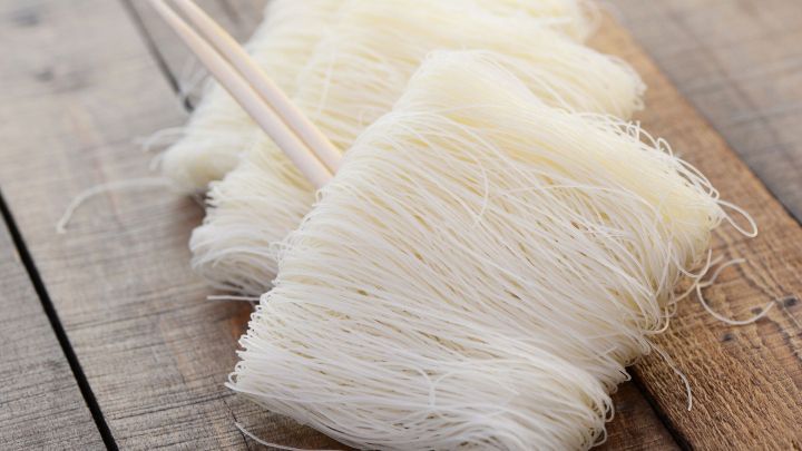 Glasnudeln liegen auf einer Holzoberfl&auml;che, w&auml;hrend Essst&auml;bchen sie leicht ber&uuml;hren, bereit zum Essen oder Kochen.