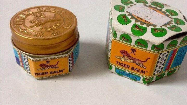 Tiger Balm-Glastiegel liegt neben passender Schachtel auf wei&szlig;em Hintergrund; beide zeigen das Tiger Balm-Logo und -Design.