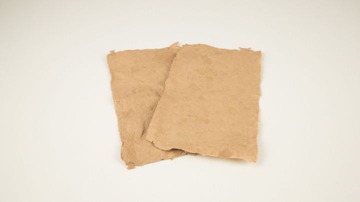 Zwei selbst gesch&ouml;pfte Papierteile liegen auf einer wei&szlig;en Oberfl&auml;che und zeigen eine unregelm&auml;&szlig;ige, nat&uuml;rliche Textur.
