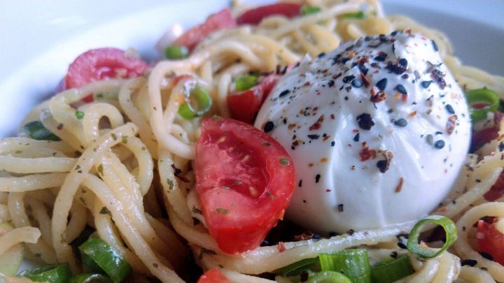 Pasta mit Burrata liegt auf einem Teller, umgeben von Tomaten und Fr&uuml;hlingszwiebeln, bereit f&uuml;r ein schnelles Abendessen.
