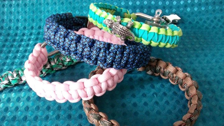Bunte Paracord-Armb&auml;nder mit Cobra-Knoten liegen auf einem blauen, strukturierten Hintergrund.