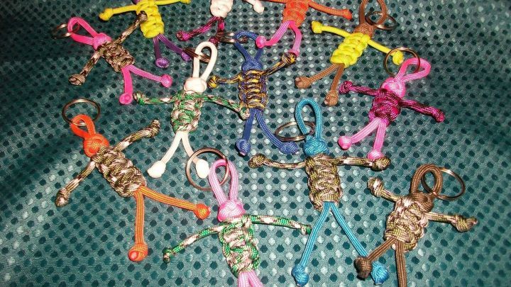 Bunte Paracord-M&auml;nnchen liegen verstreut auf einem gr&uuml;nen Stoff. Sie sind kleine Figuren mit Schl&uuml;sselringen.