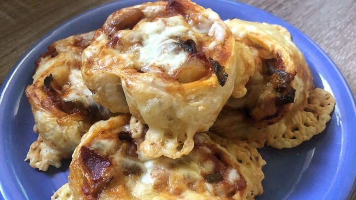 Auf einem blauen Teller liegen knusprige Pizzaschnecken mit Salami und Zucchini, goldbraun und geschmolzenem K&auml;se.