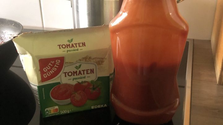 Eine Flasche mit Tomatenso&szlig;e steht neben einer Packung passierten Tomaten auf einem Herd in einer modernen K&uuml;che.