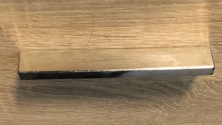 Ein M&ouml;belgriff aus Metall lehnt an einem hellen Holzregal, w&auml;hrend ein anderer darunter mit Deko-Klebeband gestaltet ist.