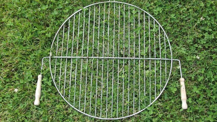 Ein Grillrost liegt auf dem gr&uuml;nen Gras. Er ist oval, mit zwei Holzgriffen und bereit zum Reinigen.