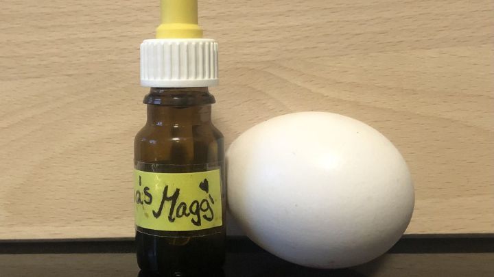 Eine kleine Flasche mit gelbem Deckel steht neben einem wei&szlig;en Ei auf einem Tisch aus hellem Holz, bereit zum Mitnehmen.