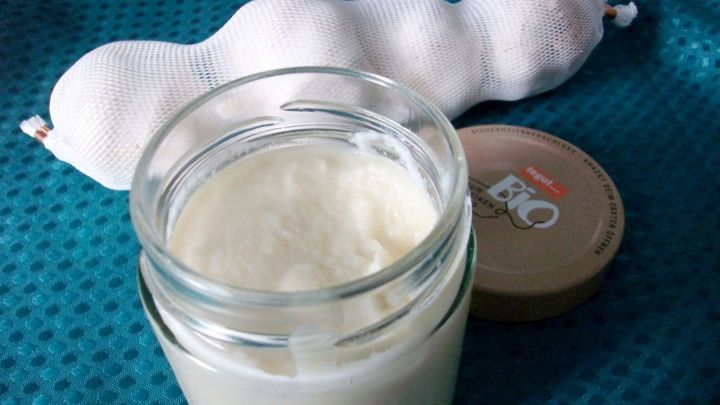 Eine Glasdose mit heller Knoblauchpaste steht auf einem blauen Tisch, w&auml;hrend frischer Knoblauch daneben liegt.