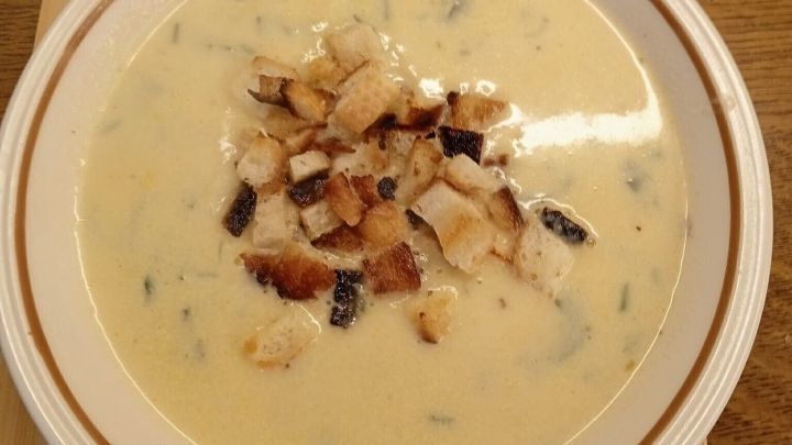 Die cremige Zucchinisuppe steht in einer Sch&uuml;ssel und ist mit ger&ouml;steten Brotst&uuml;cken garniert, auf einem Holzbrett platziert.