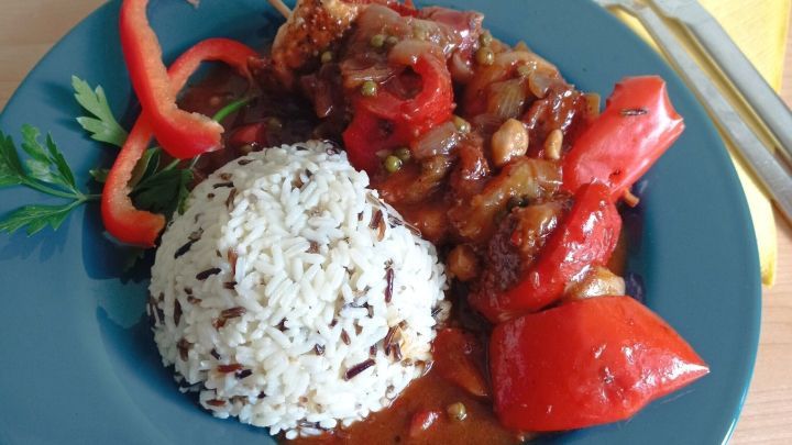 Auf einem blauen Teller liegt Putenschaschlik mit buntem Gem&uuml;se und So&szlig;e, daneben ein H&uuml;gel von Reis, umgeben von frischem Gem&uuml;se.