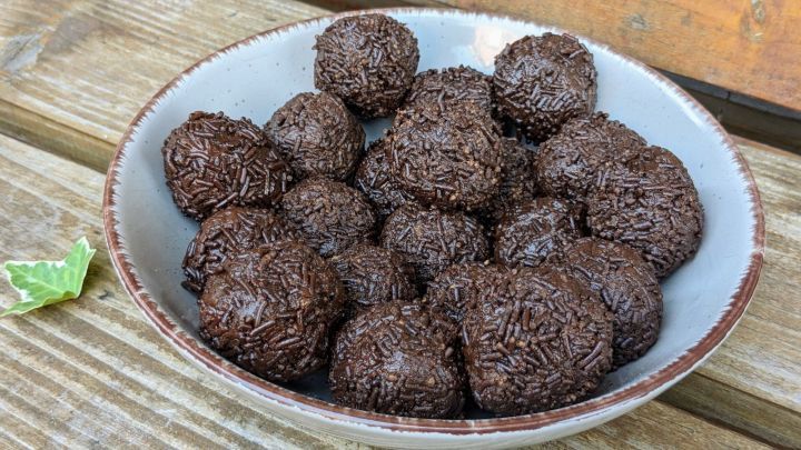 In einer Sch&uuml;ssel liegen viele gl&auml;nzende Schokokugeln, die mit Schokoladenstreuseln &uuml;berzogen sind, auf einem Holzuntergrund.