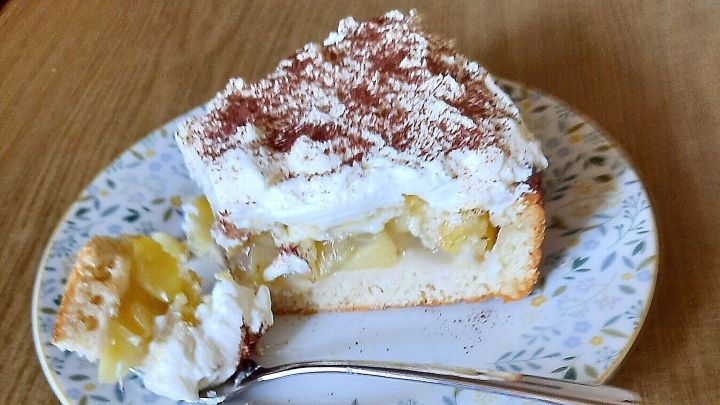Ein St&uuml;ck Weinapfeltorte mit Streuseldecke liegt auf einem blumenmusterierten Teller, daneben liegt ein L&ouml;ffel.