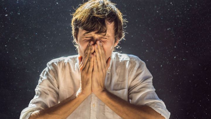 Ein junger Mann h&auml;lt sich mit beiden H&auml;nden das Gesicht zu und wirkt betroffen, umgeben von spr&uuml;hendem Wasser.