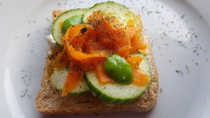 Ein vollkornbrot mit Gurkenscheiben und Karottenraspeln liegt auf einem Teller, dekoriert mit gr&uuml;nen Bohnen und Dill.