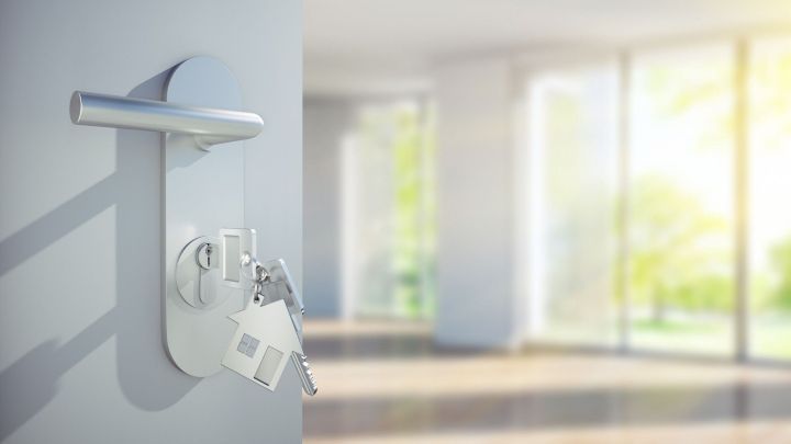 Ein Schl&uuml;sselbund mit einem Hausschl&uuml;ssel h&auml;ngt an einer silbernen T&uuml;r und &ouml;ffnet den Weg zu einem hellen, modernen Raum.