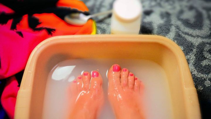 Zwei F&uuml;&szlig;e mit rosa Nagellack befinden sich in einem Wasserbecken mit Schmierseife zur Behandlung einer Nagelbettentz&uuml;ndung.