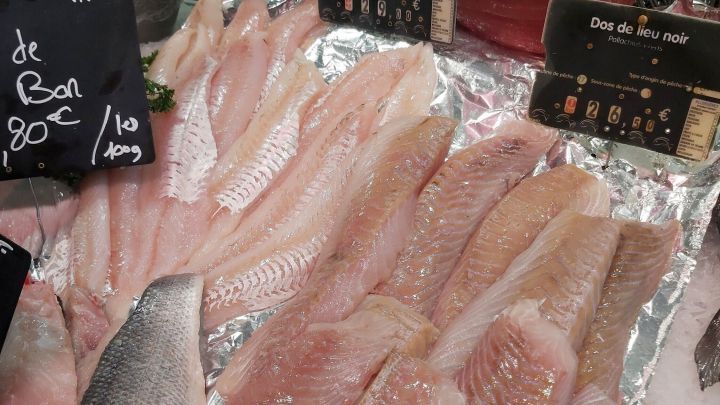 Frische Fischfilets liegen auf einem Eisteller, umgeben von Preisschildern und gr&uuml;ner Petersilie im Verkaufsbereich.