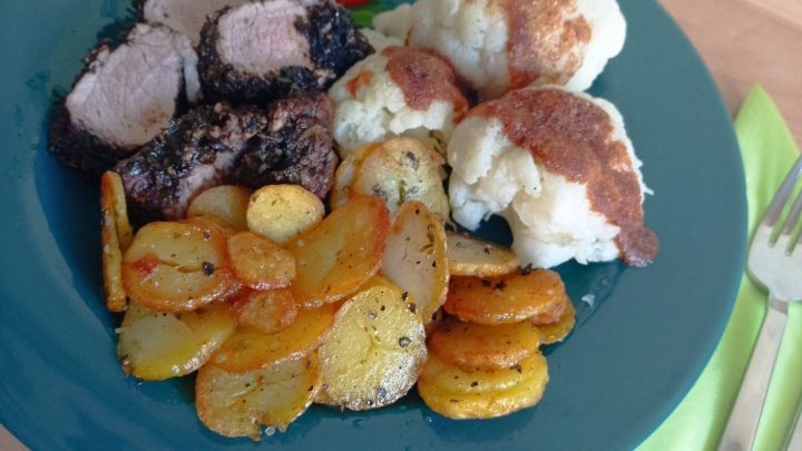 Auf einem blauen Teller liegt mariniertes Schweinefilet, umgeben von gebratenen Kartoffeln und Blumenkohl.