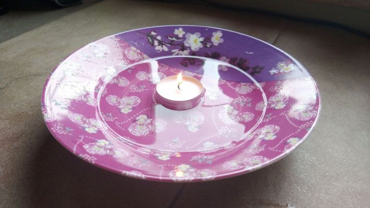 Eine lila-bunte Schale mit einer kleinen Kerze in der Mitte steht auf einem Tisch, um Fl&ouml;he mit W&auml;rme anzulocken.