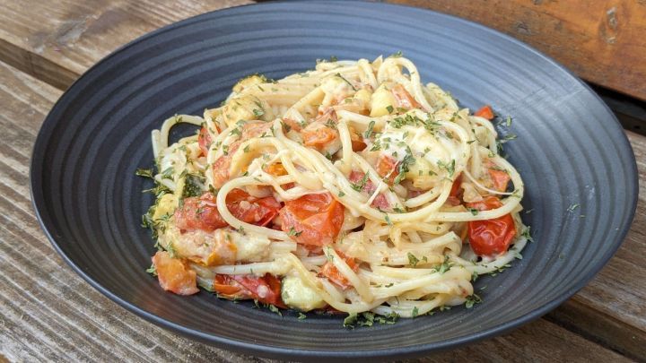 Eine schwarze Schale enth&auml;lt k&ouml;stliche Pasta mit Ofengem&uuml;se, garniert mit frischen Kr&auml;utern, auf rustikalem Holz.