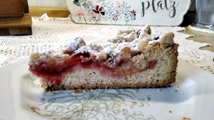 Ein St&uuml;ck Zwetschgenkuchen liegt auf einem dekorativen Teller, staubzuckerbest&auml;ubt, in einer gem&uuml;tlichen Umgebung mit einem einladenden Tisch.