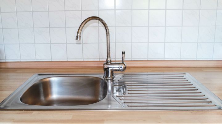 Ein gl&auml;nzendes Sp&uuml;lbecken steht bereit zum Reinigen. Die Umgebung ist eine moderne K&uuml;che mit Fliesen und Holz.