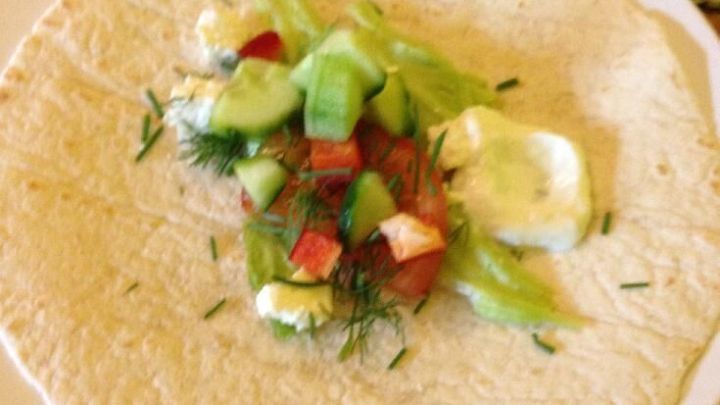 Ein Wrap liegt auf einem Teller, gef&uuml;llt mit frischem Gem&uuml;se und H&uuml;ttenk&auml;se, bereit zum Rollen in einer gem&uuml;tlichen K&uuml;che.