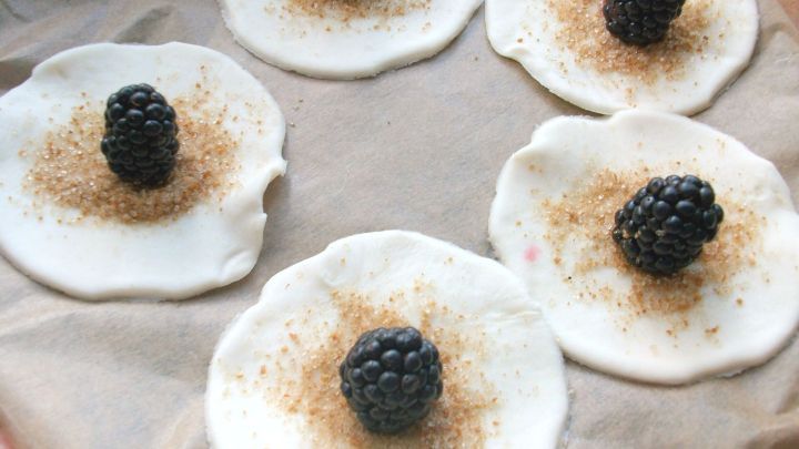Runde Bl&auml;tterteigst&uuml;cke sind mit Zucker bestreut und haben jeweils eine Brombeere in der Mitte platziert.