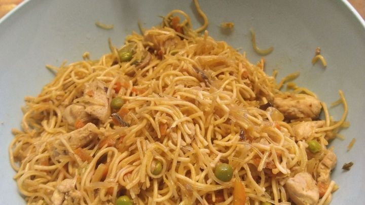 Eine gro&szlig;e Sch&uuml;ssel mit gebratenen Nudeln zeigt zarte Nudeln, Gem&uuml;se und H&uuml;hnchen in einer K&uuml;che.