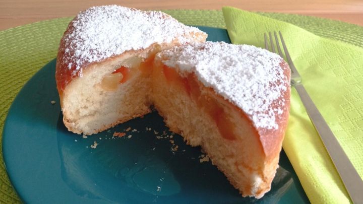 Buchteln mit Apfelf&uuml;llung liegen auf einem blauen Teller, der auf einer gr&uuml;nen Tischdecke steht. Eine H&auml;lfte ist aufgeschnitten.