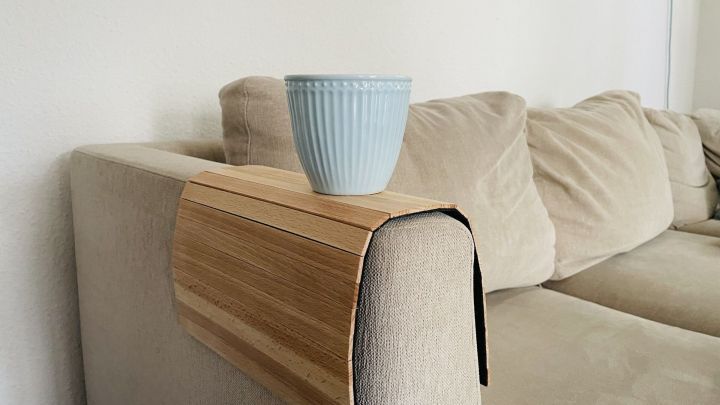 Ein rustikales Sofatablett steht auf der Armlehne eines beigen Sofas und h&auml;lt einen blauen Blumentopf.