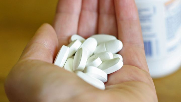 Eine Hand h&auml;lt mehrere wei&szlig;e Tabletten, die gegen Wadenkr&auml;mpfe helfen k&ouml;nnen, im Hintergrund steht eine Flasche.