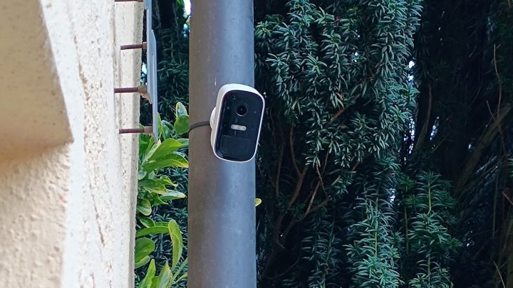 Eine &Uuml;berwachungskamera ist an einem Pfosten montiert und &uuml;berwacht den umgebenden Garten mit B&auml;umen.